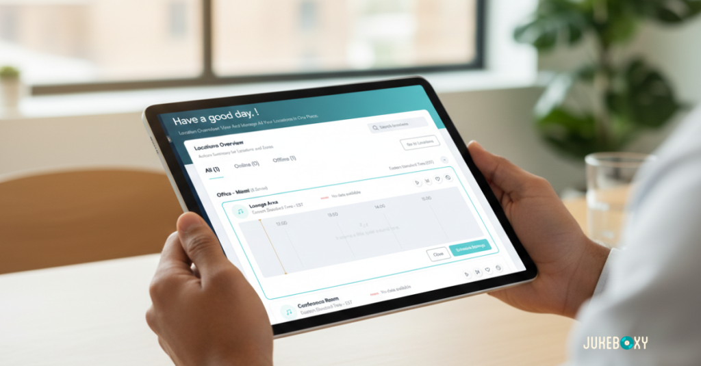 A person holding a tablet in a modern office, displaying the Jukeboxy music management dashboard with a 'Have a good day!' greeting and location overview.