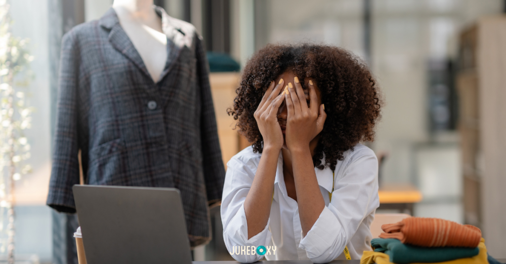 A stressed female business owner sitting at a desk with her hands over her face, representing the legal risks of unlicensed music in a retail setting.