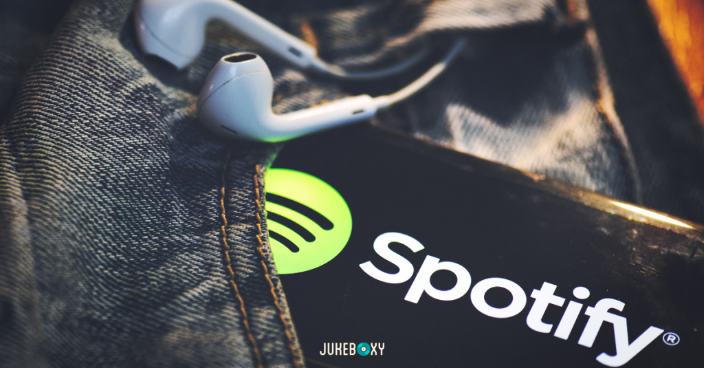 A smartphone in a denim pocket displaying the Spotify app logo next to white earbuds, illustrating personal music use that is not licensed for businesses.