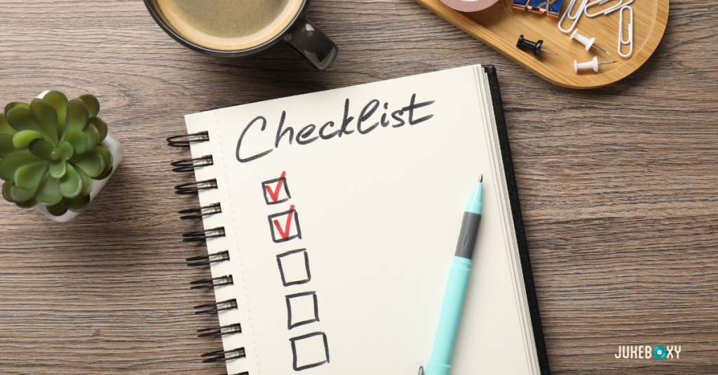 An overhead view of a notebook with the word "Checklist" written at the top and red checkmarks in boxes, placed on a wooden desk next to a coffee cup and a succulent.