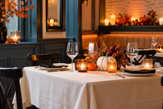Restaurant dining room decorated for Halloween with mini pumpkins, candles and autumn leaves on white tablecloths