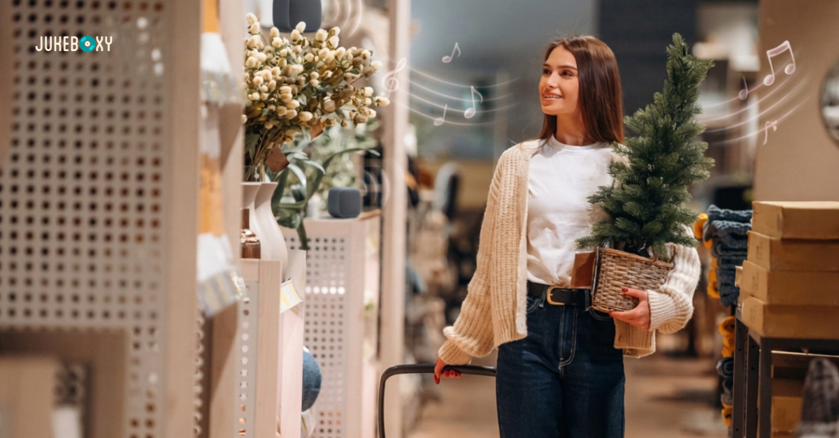 **Alt text:** Smiling shopper carrying a small Christmas tree in a retail store with background music playing from shelf speakers